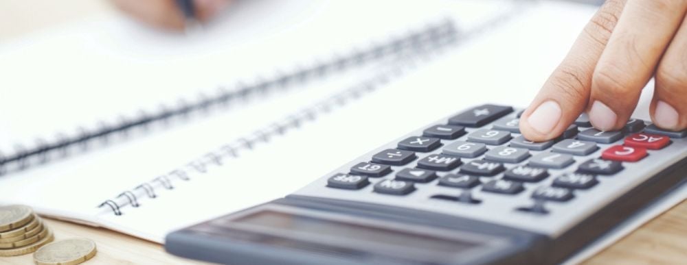 Individuo consultando documentos financieros y utilizando una calculadora para evaluar su capacidad de endeudamiento, con folletos de Tu Casa Más en la mesa, planificando la compra de su próxima casa.